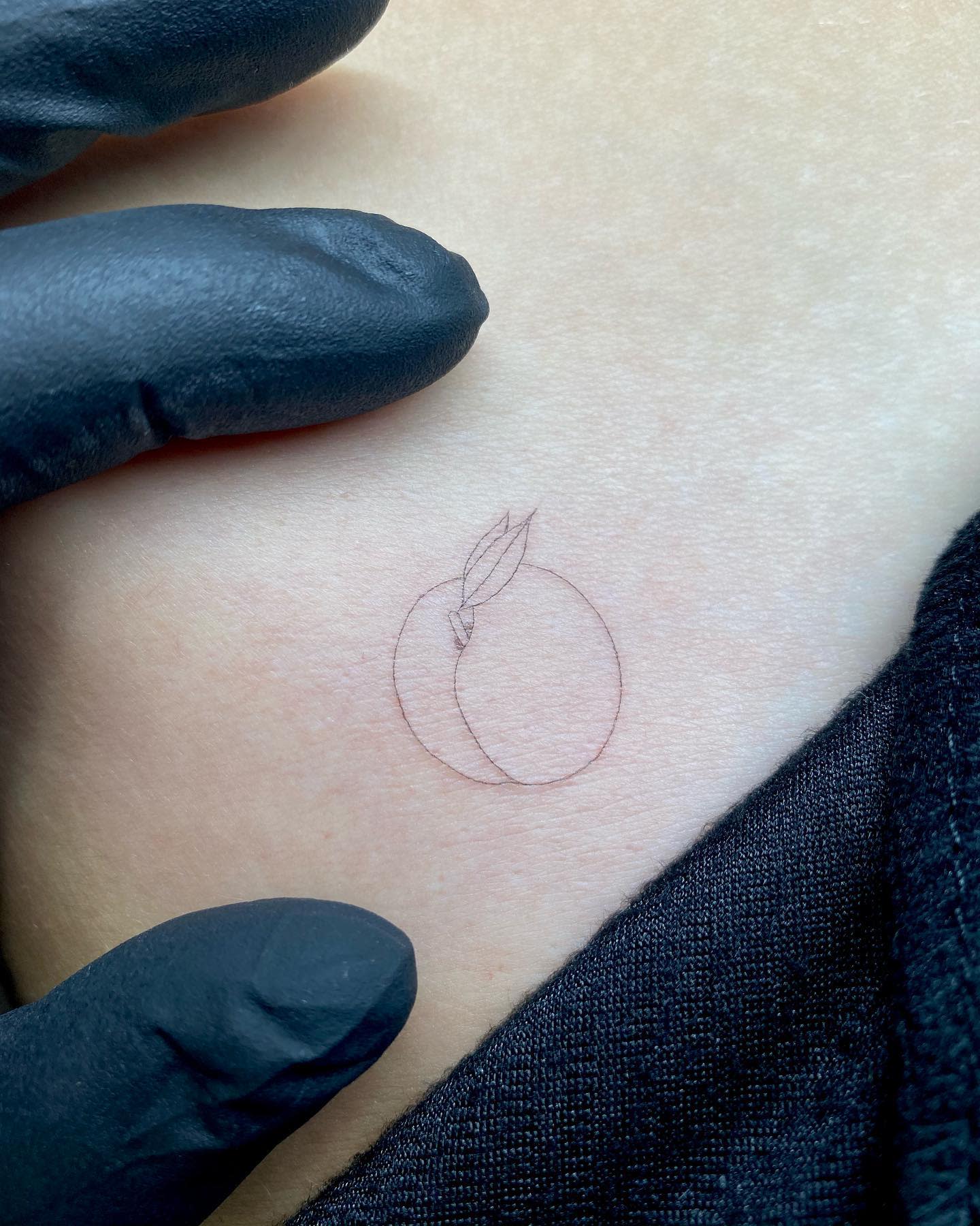 Outline tattoo of a peach with a leaf